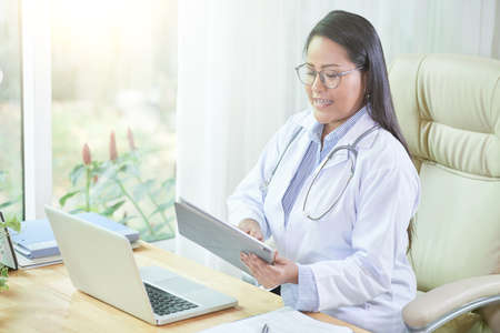 Female medical worker reading information on digital table when working in officeの写真素材