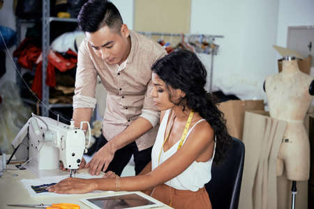 Team of young tailors trying to use new sewing machine for the first timeの写真素材