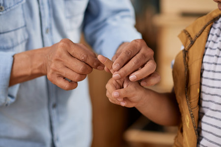 Close-up image of father applying band-aid on injured finger of his son