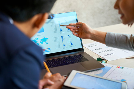 Financial managers pointing at chart on screen and discussing consistent development of company at...