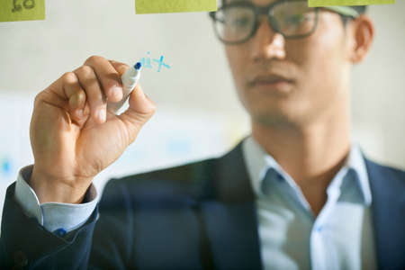 Young Asian businessman writing on glass wall with markerの写真素材