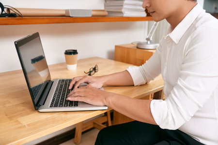 Cropped image of businessman sitting at tablet and answering e-mails on laptop