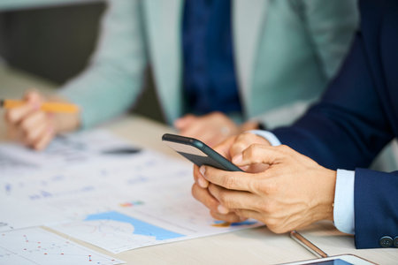 Hands of businessman texting friends or colleagues when sitting at meeting table