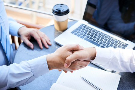 Close-up of two businessmen have a meeting and shaking hands while sitting at the table with laptop...