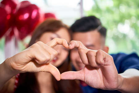 Portrait of young lovely couple making heart shape from their hands and smilingの写真素材