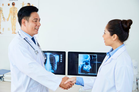 Two medical colleagues standing in lab coats and shaking hands to each other, they cooperating in...