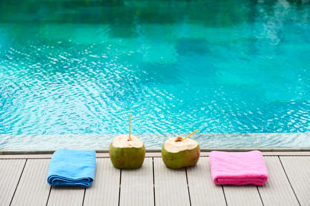 Image of two coconut drinks and two colorful towels at poolside outdoorsの写真素材
