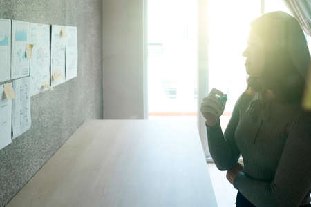 Young businesswoman standing at office and looking at wall with financial documentsの写真素材