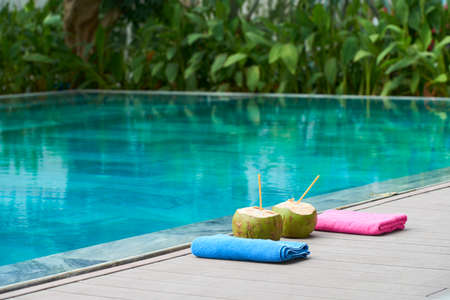 Two fresh drinks in coconuts and towels served near the swimming pool outdoors at resortの写真素材