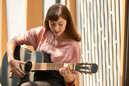 Smiling pretty young woman singing a song and playing guitar