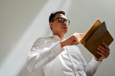 Young handsome Vietnamese entrepreneur reading important information on digital tablet