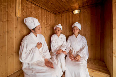 Group of Asian beautiful women wearing white bathrobes and towels on their heads taking a sauna togetherの写真素材