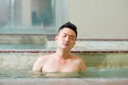 Asian man with eyes closed has water procedure in the swimming pool at spa centreの写真素材