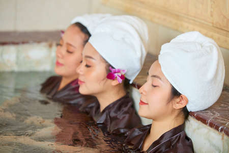 Group of young Asian girls with towel on their heads sitting in the water with eyes closed and relaxingの写真素材
