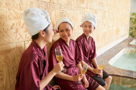 Happy female friends celebrating with champagne and talking to each other at luxury spa centre