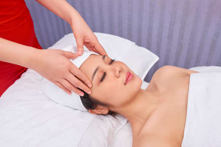 Young beautiful woman relaxing on bed with eyes closed and having procedure for face at spa salonの写真素材