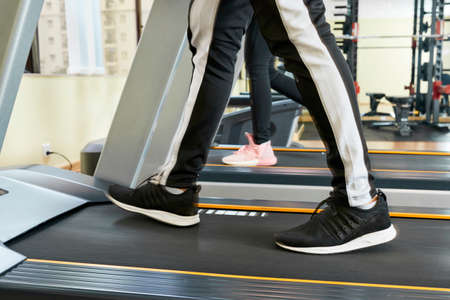 Close-up of man in sport trousers and sneakers walking on treadmill in gymの写真素材