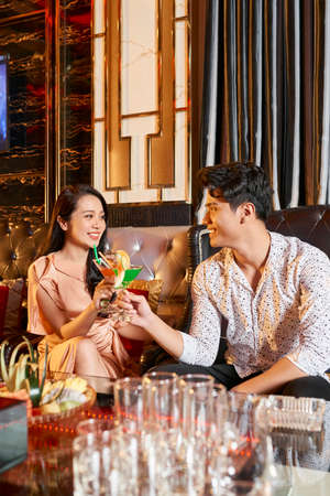 Young happy couple sitting at the table at restaurant and toasting with cocktails, they celebrating their anniversaryの写真素材