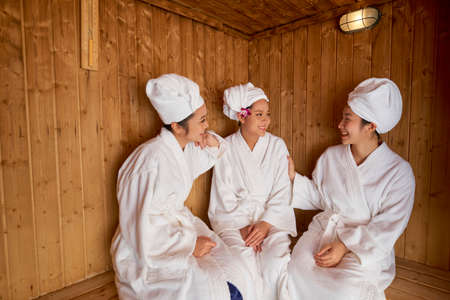 Group of happy female friends take care of their health and bodies in wooden sauna room at spa centerの写真素材