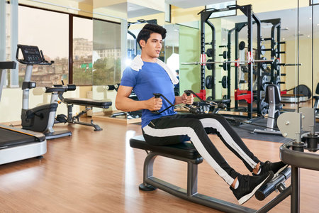Young Asian man in sports clothing training on sport equipment in modern gym
