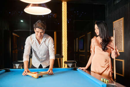 Asian young couple standing near the billiard table and playing billiard in pubの写真素材