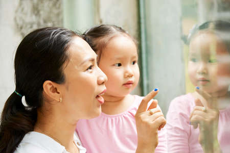 Young Vietnamese woman pouring at cage in zoo and telling daughter about animalsの写真素材