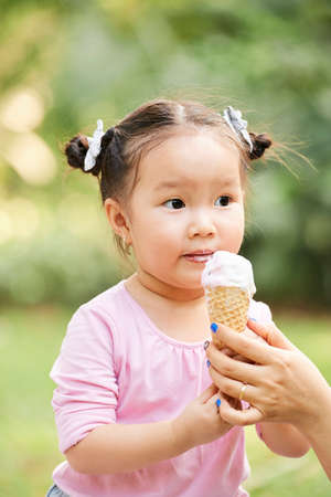 Mother giving ice cream to her cute little daughter with beaded hairの写真素材
