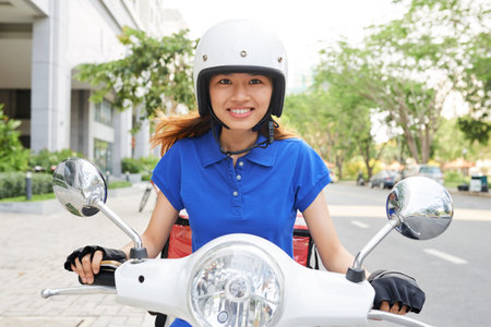 Portrait of female happy food courier on scooter in hurry to deliver lunch