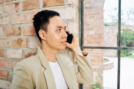 Handsome young entrepreneur looking through office window when talking on phone