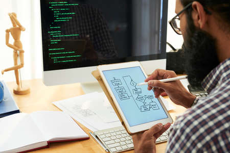 Office worker sitting at his workplace in front of computer monitor and drawing business strategy on display of digital tablet at officeの写真素材