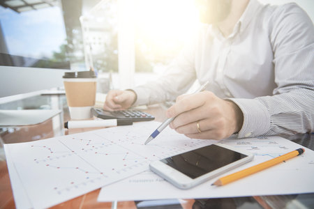 Close-up of office worker pointing at document with charts and analyzing it while working at his...