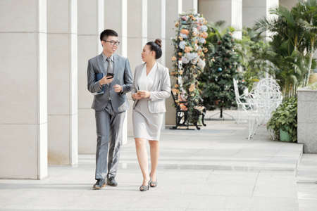 Young business people holding mobile phones and talking to each other while walking together in the cityの写真素材