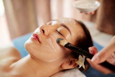 Face of young Asian woman getting moisturizing face treatment in beauty salonの写真素材