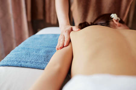 Masseurs hands massing slim back of young woman in spa salonの写真素材