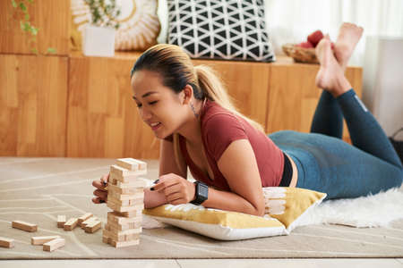 Lovely smiling young woman building tower out of wooden blockの写真素材