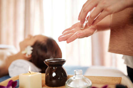 Masseur putting oil in hands to warm it up before applyingon face of female clientの写真素材