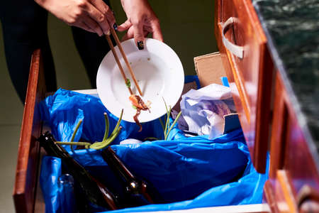 Hands of woman putting food leftovers into container for organic waste at homeの写真素材