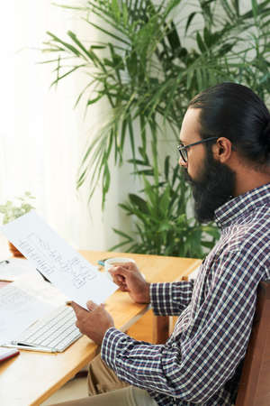 Serious bearded manager sitting at office desk examining and developing new business planの写真素材