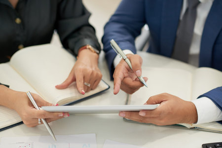 Close-up of business people sitting at the table pointing at display of digital tablet and...