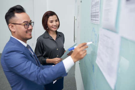Two Asian business colleagues standing near the whiteboard and preparing for business presentation together while standing at officeの写真素材