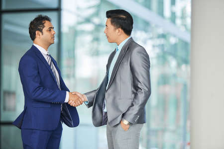 Two businessmen in suits standing outdoors near the entrance in office building and shaking hands to each otherの写真素材