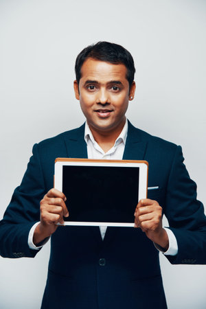 Portrait of confident male executive in suit holding digital tablet with blank display and showing...