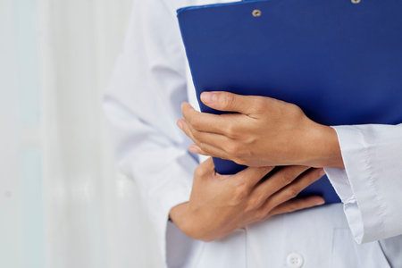 Close-up of female doctor standing in white coat holding blue folder at hospital