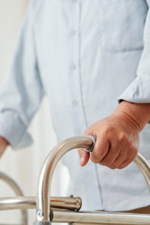 Close-up of senior man trying to walk with walker along the corridor at hospital