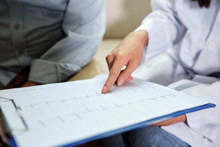 Close-up of cardiologist pointing at clipboard with cardiogram and showing it to senior patient...