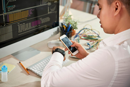 Serious young businessman sitting at the table in front of computer monitor with software and using...