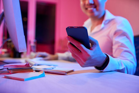 Close-up of young man sitting at workplace holding mobile phone in his hand and answering on the...