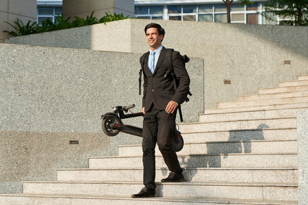 Smiling young office worker in formal wear and with backpack behind his back holding scooter while...