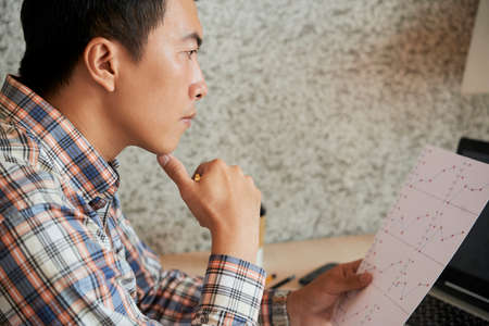 Contemplating mature Asian entrepreneur checking document with financial chartの写真素材