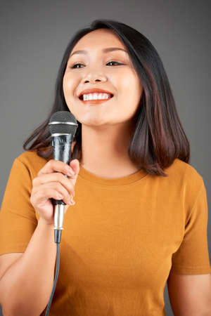 Happy young Asian woman with microphone singing song or telling story on microphoneの写真素材